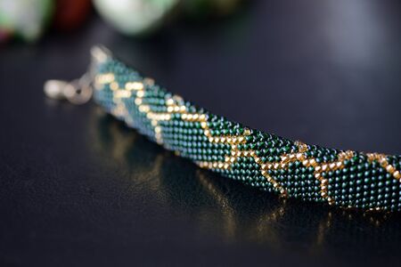 Dark green beaded necklace with golden print on a dark background close upの写真素材