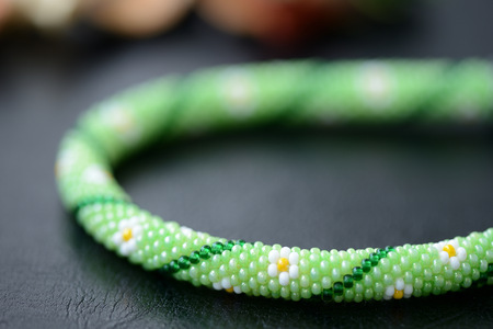 Green summer necklace with chamomile print on a dark background close upの写真素材