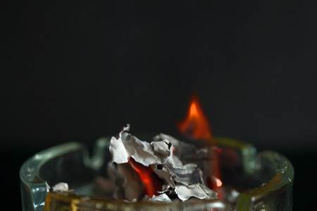 A piece of paper burning down in a glass ashtray close upの写真素材