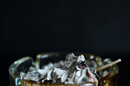 A piece of paper burning down in a glass ashtray close up