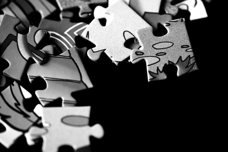 Pieces of children's puzzles scattered on a dark background close up. Black and white