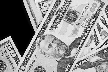 A pack of fifty dollar bills on a dark background. Black and white