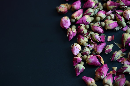 Dried rose buds scattered on a dark surface close upの写真素材