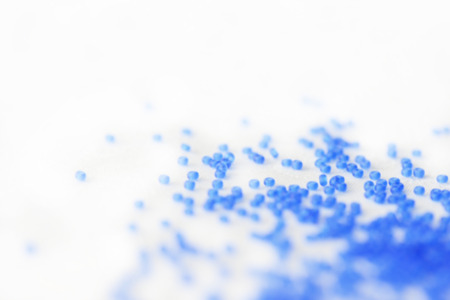 Seed beads of blue color scattered on textile background close up