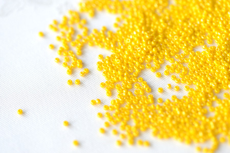 Seed beads yellow color scattered on a textile background close upの写真素材