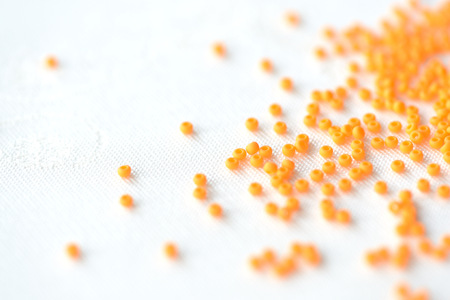 Opaque seed beads orange color scattered on a textile background close upの写真素材