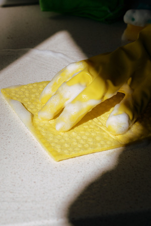 Hand in yellow rubber glove washing surface on a sunny day. Spring cleaning	brown color tonedの写真素材