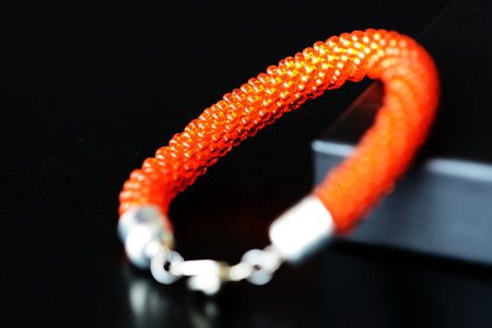 Orange color beaded bracelet made of transparent seed beads on a dark background close upの写真素材