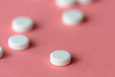 White tablets scattered on a pink background close upの写真素材