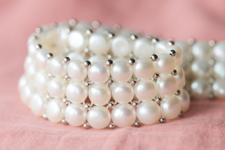 Beautiful white pearl necklace on a coral color textile background close upの写真素材