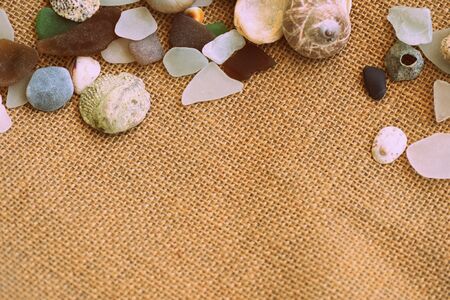 Shells, sea glasses and stones on a jute background close-up brown color toned. Vacation concept