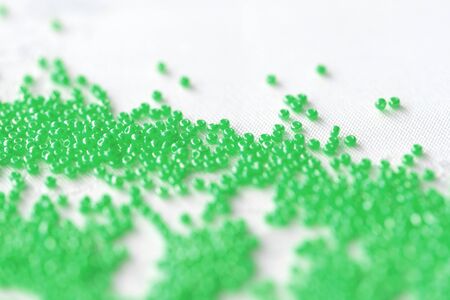 Seed beads green color scattered on a white textile background close up