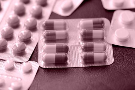 Pills and tablets blisters scattered on a dark background close up pink color toned