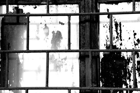 Old window painted white paint behind a rusty bars closeup, black and white