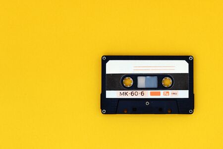 Old audio tape cassette on a bright yellow background. Top view, old technology concept