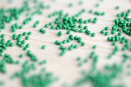 Closeup of green seed beads scattered on a wooden surfaceの写真素材