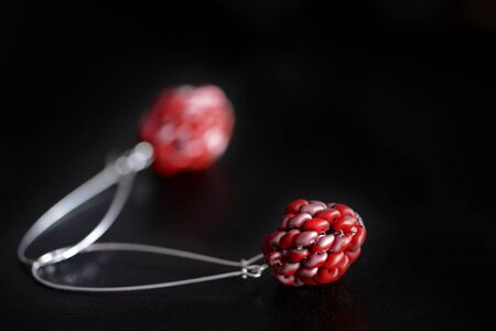 Red dangle earrings made of superduo beads on a dark background close-up