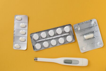 Thermometer and blisters of pills on a bright yellow background. Flat lay, top view. Pharmacy and...