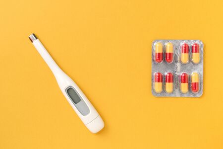 Thermometer and blister with pills on a bright yellow background. Flat lay, top view. Pharmacy and...