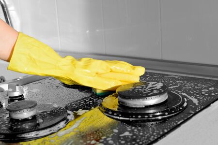 A hand in a yellow rubber glove washes a gas stove. Black and white, selective colorの写真素材