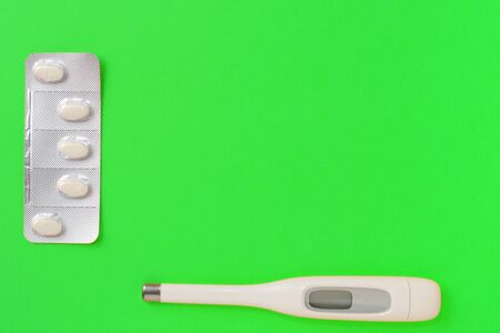 Pills and thermometer on a green background. Flat lay, top view, copy space. Pharmacy concept