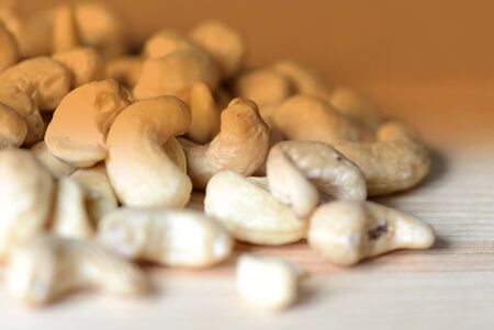 Cashew nuts scattered on a wooden surface close-up. Healthy food background. Brown color toned