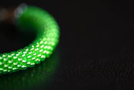Fragment of a green beaded bracelet on a dark surface close-up. Fashion backgroundの写真素材