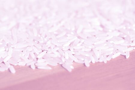 White rice grains scattered on a wooden surface close up. Food background pink color tonedの写真素材