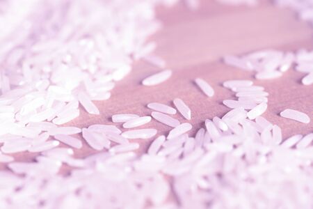 White rice grains scattered on a wooden surface close up. Food background pink color toned