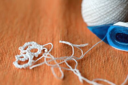 Tatting lace in the manufacturing process. Fragment of lace and shuttle on textile background...