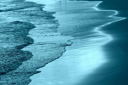 The coastal sand washed by the waves lit by the evening sun. Natural abstract background blue color tonedの写真素材