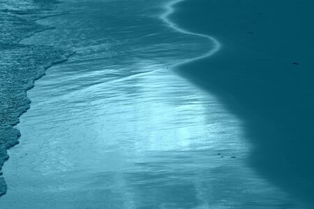 The coastal sand washed by the waves lit by the evening sun. Natural abstract background blue color tonedの写真素材