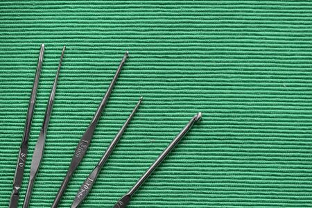 Set of metal crochet hooks on a green textile background close-up. Handmade concept. Top view, copy spaceの写真素材