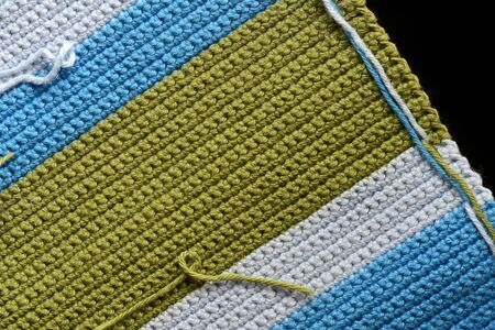 Fragment of crocheted fabric from green, blue and light blue threads close-up, top view. Abstract...