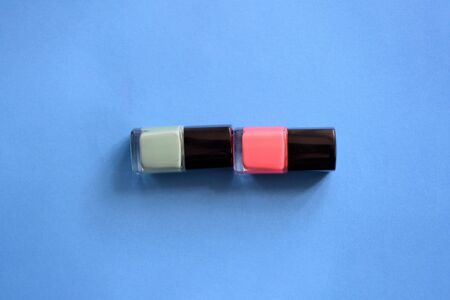 Two bottles with pink and mint color nail polish on a blue background. Top view, copy space. Manicure art cosmetic concept. Nail artの写真素材