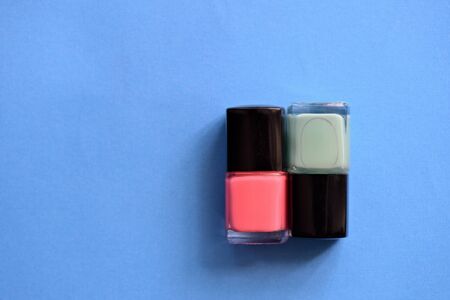 Two bottles with pink and mint color nail polish on a blue background. Top view, copy space. Manicure art cosmetic concept. Nail artの写真素材