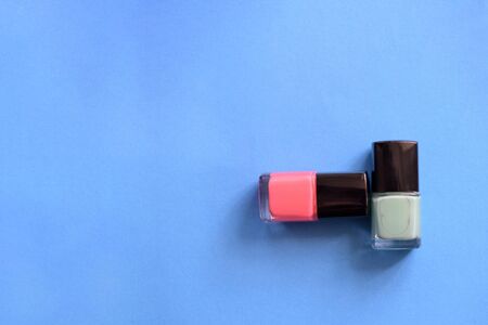 Two bottles with pink and mint color nail polish on a blue background. Top view, copy space. Manicure art cosmetic concept. Nail artの写真素材