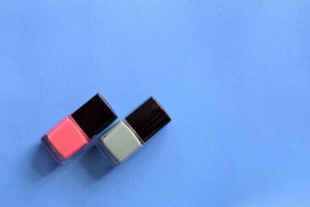 Two bottles with pink and mint color nail polish on a blue background. Top view, copy space. Manicure art cosmetic concept. Nail artの写真素材