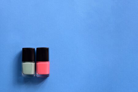 Two bottles with pink and mint color nail polish on a blue background. Top view, copy space. Manicure art cosmetic concept. Nail artの写真素材