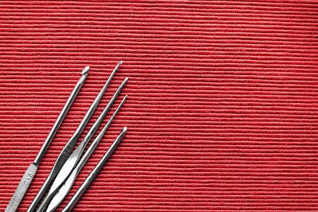 Metal crochet hooks on a red background close-up.  Top view, copy space. Handmade conceptの写真素材