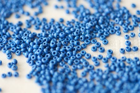 Seed beads blue color scattered on a textile background close-up. Handmade, art, creativityの写真素材