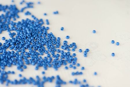 Blue seed beads scattered on a white textile background closeup. Handmade conceptの写真素材