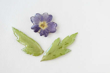 Blue flower and green leaves filled with epoxy resin on a white textile background, top view. The basis for a pendant or earrings. Handmade jewelry in the manufacturing processの写真素材