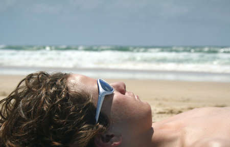 Teenage boy sun tanning on the beachの写真素材