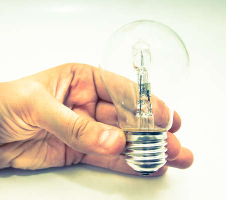 A hand holding a lightbulb against white background