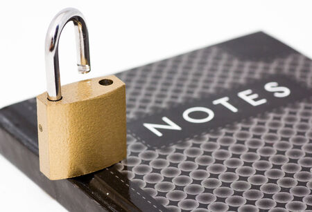 A padlock standing on a closed notepad isolated on whiteの写真素材