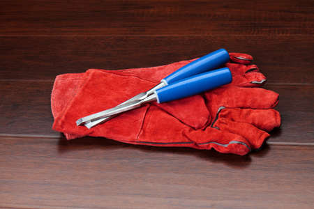 Red gloves and blue chisels on dark wooden floorの写真素材
