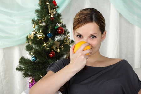 The young beautiful woman sits near a christmas fur-tree and eat an orangeの写真素材