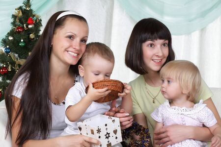 Two mums and their kids sits near a christmas fur-treeの写真素材
