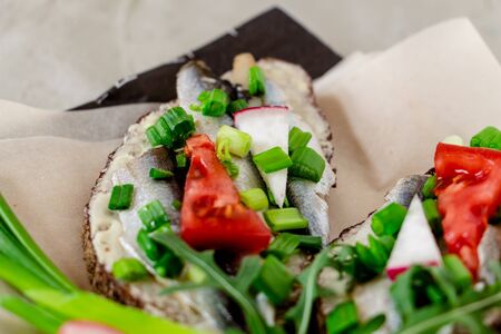 delicious sandwiches with rye bread, butter, small sardines, slices of tomatoes, radishes and green onions on food parchment on a concrete background, unusual stylish presentation of the dishの写真素材